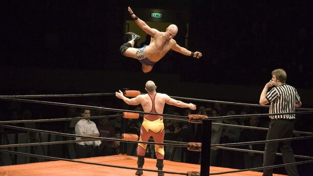 Bild från en match i amerikansk wrestling. Den ena mannen flyger i luften för att hoppa på den andre.