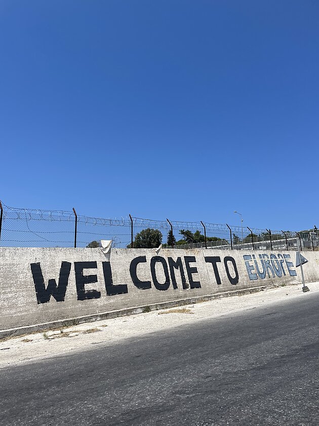 Före detta flyktinglägret Mória, Lesbos, Grekland. Graffititext på det tidigare betongstaketet lyder ”Weolcome to Europe”, 1 augusti 2023. Foto: Dianne van den Bosch.