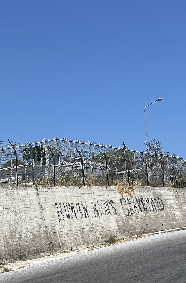 Före detta flyktinglägret Mória, Lesvos, Grekland. Graffititext på det tidigare betongstaketet lyder ”Human Rights Graveyard”, 1 augusti 2023. Foto: Dianne van den Bosch.